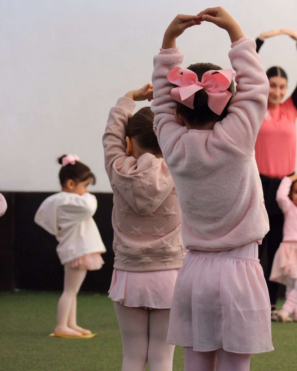 Pequeñas bailarinas practicando con los brazos en alto en Tiny Dancers